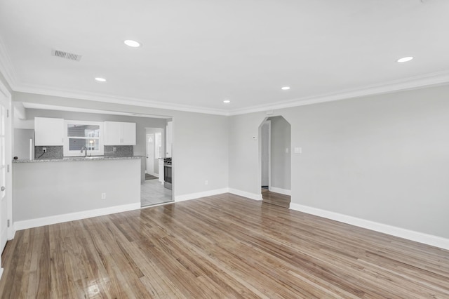 unfurnished living room with light wood-type flooring, visible vents, arched walkways, and crown molding