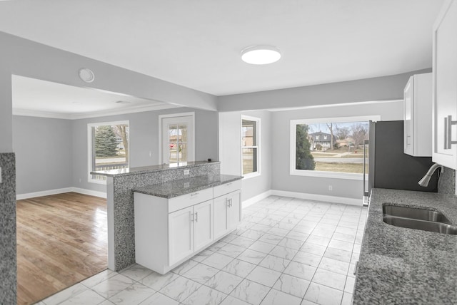 kitchen with dark stone counters, a sink, marble finish floor, baseboards, and white cabinetry