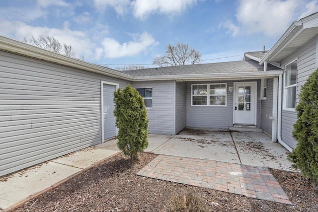 property entrance with a shingled roof and a patio