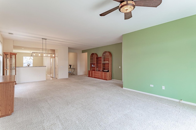 unfurnished living room with carpet flooring, baseboards, and a ceiling fan