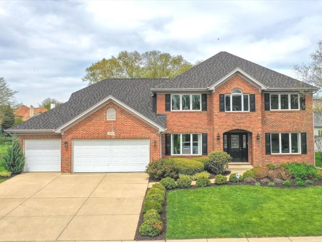 colonial-style house featuring a front yard, roof with shingles, brick siding, concrete driveway, and an attached garage