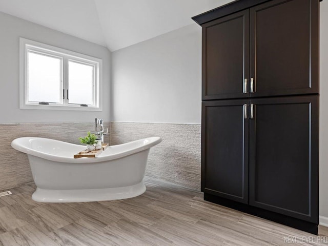 bathroom featuring vaulted ceiling, tile walls, a soaking tub, and wainscoting