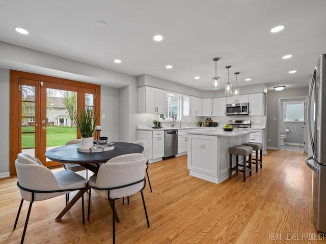 kitchen featuring white cabinets, appliances with stainless steel finishes, light countertops, light wood-style flooring, and a center island