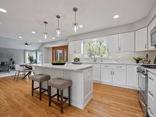 kitchen featuring a kitchen island, appliances with stainless steel finishes, a sink, a breakfast bar, and white cabinetry