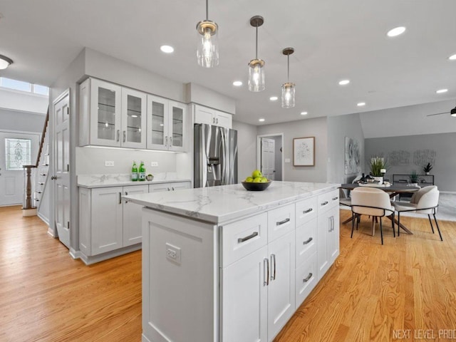kitchen featuring a kitchen island, decorative light fixtures, open floor plan, stainless steel fridge, and light wood-style flooring