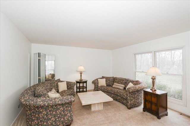 living room with light carpet, a healthy amount of sunlight, visible vents, and baseboards