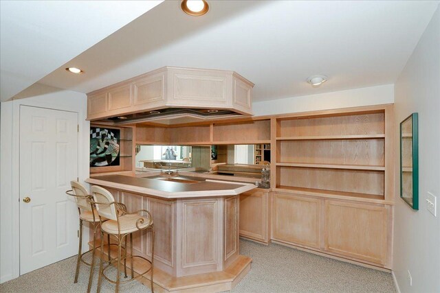 kitchen with light brown cabinets, a kitchen breakfast bar, light colored carpet, and a peninsula
