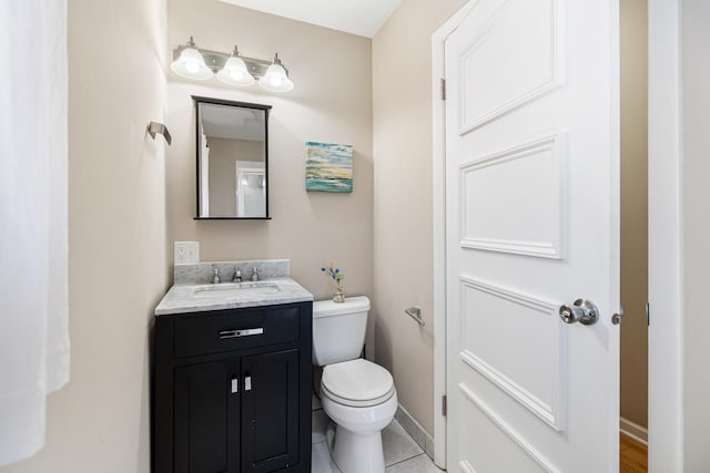 half bath featuring baseboards, vanity, tile patterned flooring, and toilet