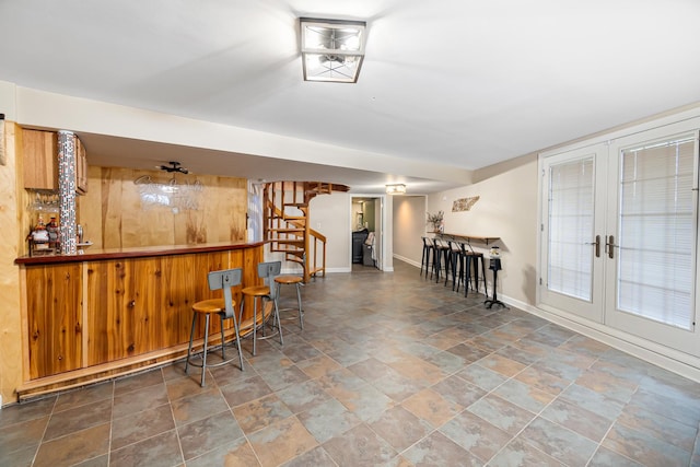 bar featuring french doors, baseboards, a bar, stone finish floor, and stairway