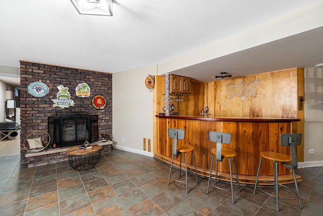 bar with stone finish floor, visible vents, a dry bar, baseboards, and a brick fireplace