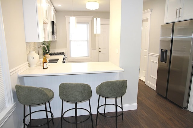 kitchen featuring stainless steel appliances, a peninsula, a sink, dark wood-style flooring, and a breakfast bar area