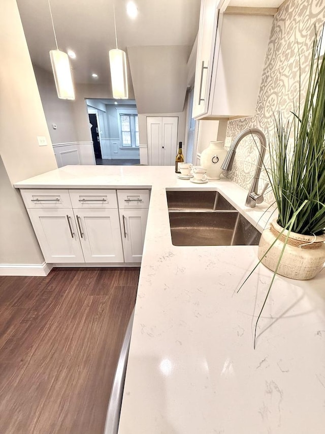 kitchen featuring dark wood-style floors, light stone counters, a sink, decorative light fixtures, and white cabinetry