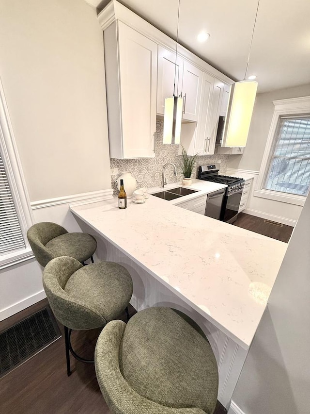 kitchen with white cabinets, dark wood-style floors, stainless steel gas stove, visible vents, and a sink