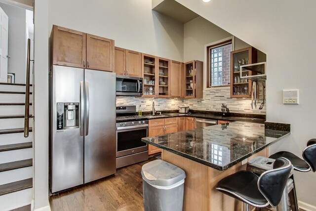 kitchen with a sink, dark wood finished floors, stainless steel appliances, a peninsula, and tasteful backsplash