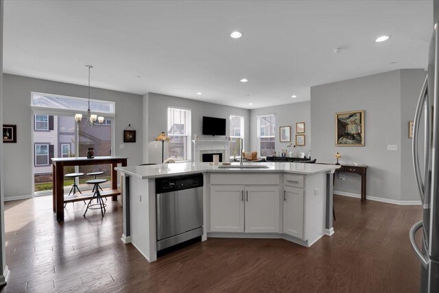 kitchen with dark wood finished floors, a kitchen island with sink, stainless steel appliances, light countertops, and a sink