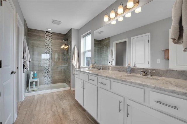 full bath with a sink, double vanity, visible vents, a stall shower, and wood finished floors