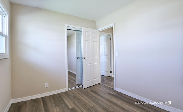 unfurnished bedroom featuring baseboards, dark wood finished floors, and a closet