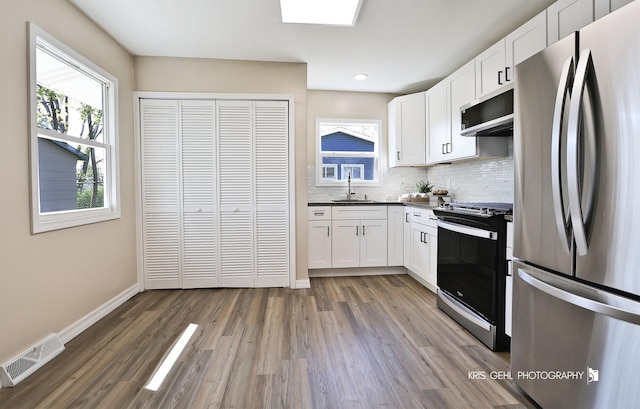 kitchen featuring white cabinets, appliances with stainless steel finishes, light wood-style floors, decorative backsplash, and visible vents