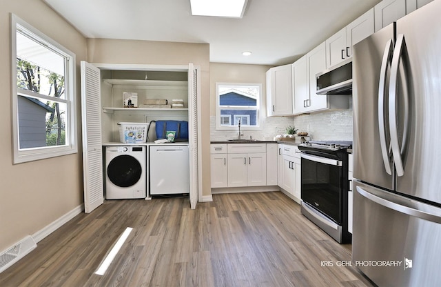 kitchen with visible vents, appliances with stainless steel finishes, a sink, white cabinets, and washer and dryer
