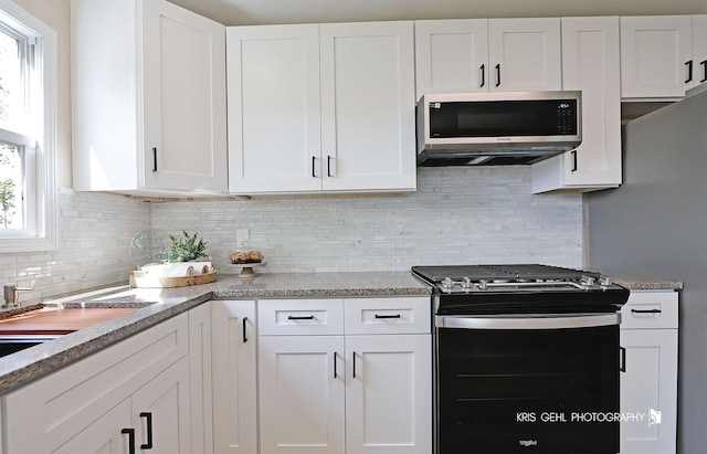 kitchen with white cabinets, light stone counters, stainless steel microwave, decorative backsplash, and gas range oven
