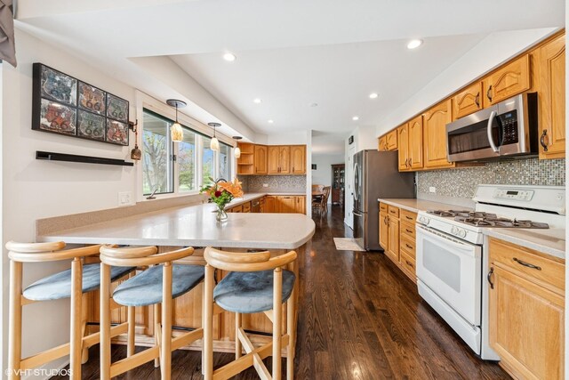 kitchen featuring decorative backsplash, a breakfast bar, a peninsula, appliances with stainless steel finishes, and dark wood-style floors