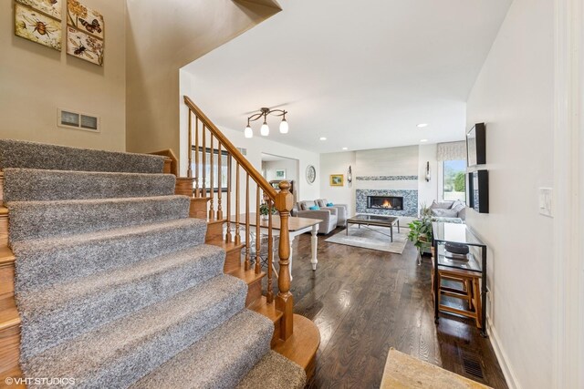 staircase featuring baseboards, a lit fireplace, wood finished floors, and visible vents