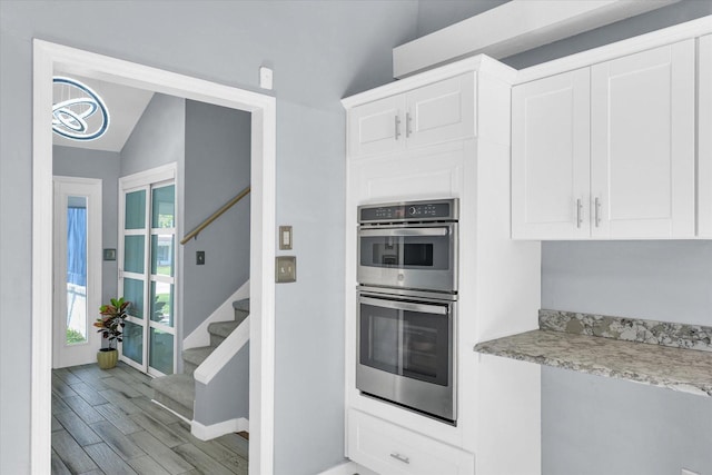 kitchen featuring lofted ceiling, stainless steel double oven, white cabinetry, baseboards, and light wood-type flooring