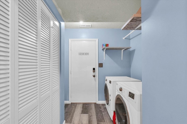 clothes washing area featuring washing machine and clothes dryer, a textured ceiling, wood finished floors, and baseboards