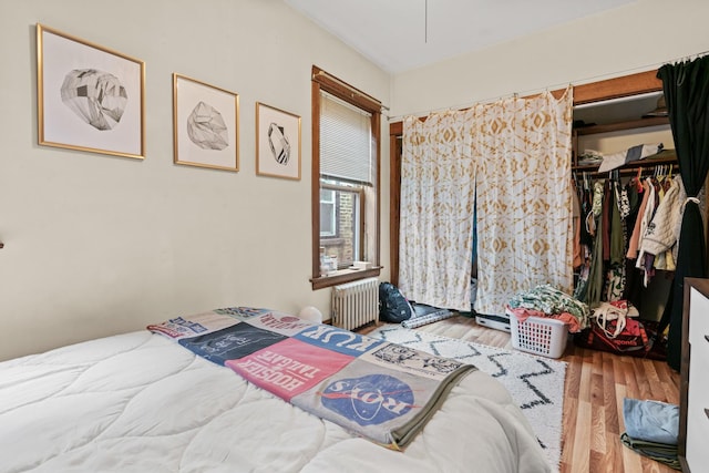 bedroom featuring a spacious closet, radiator heating unit, a closet, and wood finished floors