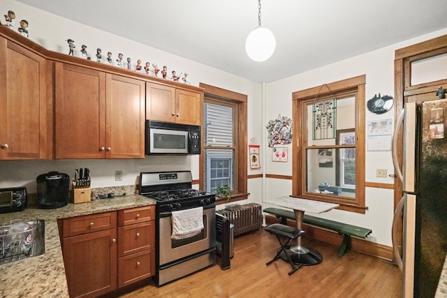 kitchen with stainless steel range with gas cooktop, light wood-style flooring, freestanding refrigerator, and brown cabinetry