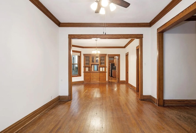 interior space featuring crown molding, ceiling fan with notable chandelier, baseboards, and wood-type flooring