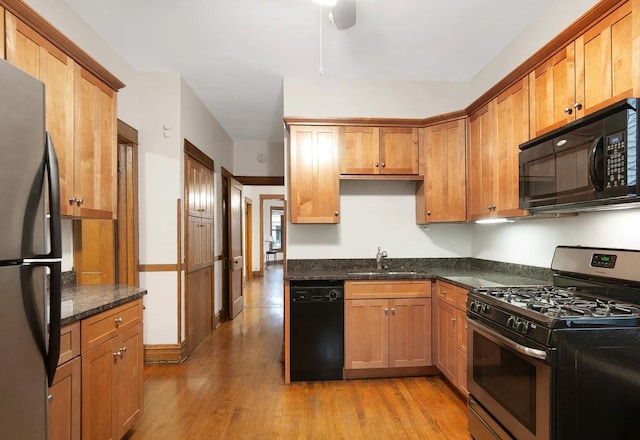 kitchen featuring light wood-style flooring, a sink, dark stone counters, brown cabinetry, and black appliances