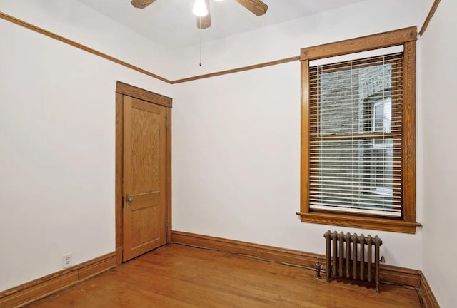 spare room featuring radiator heating unit, a ceiling fan, baseboards, and light wood-type flooring