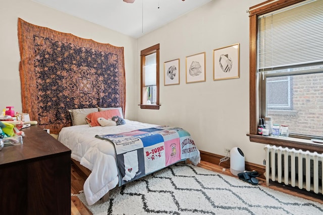 bedroom with radiator heating unit, baseboards, wood finished floors, and ceiling fan