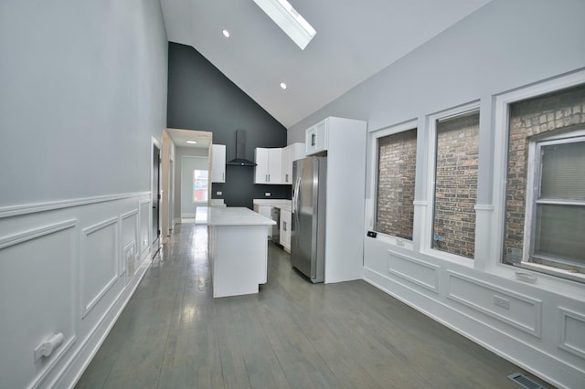 kitchen with light countertops, freestanding refrigerator, wall chimney exhaust hood, a skylight, and white cabinetry