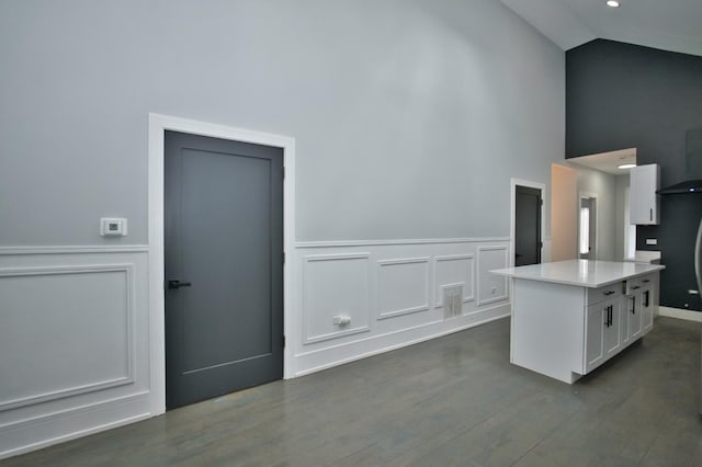 interior space featuring high vaulted ceiling, a decorative wall, light countertops, white cabinets, and dark wood-type flooring