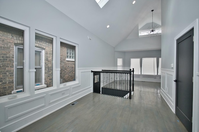 hallway with visible vents, a decorative wall, wainscoting, high vaulted ceiling, and dark wood-style flooring