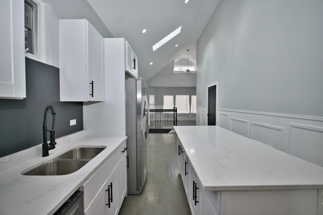 kitchen with a sink, freestanding refrigerator, a skylight, wood finished floors, and a kitchen island