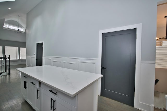 kitchen with white cabinets, dark wood-style floors, light stone counters, a center island, and wainscoting