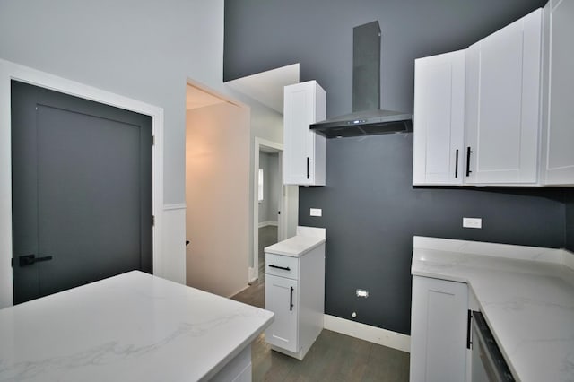 kitchen with wood finished floors, wall chimney exhaust hood, white cabinetry, and light stone counters