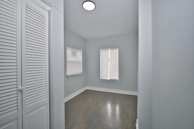 unfurnished bedroom with a closet, baseboards, and dark wood-style flooring