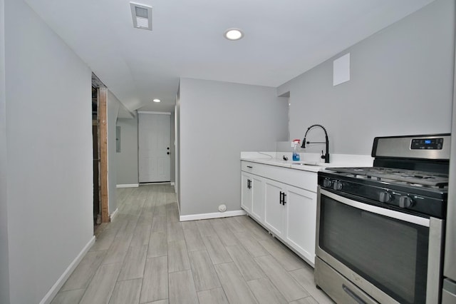 kitchen featuring white cabinets, visible vents, a sink, stainless steel range with gas cooktop, and baseboards