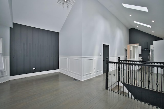 additional living space with high vaulted ceiling, a decorative wall, wood finished floors, a skylight, and recessed lighting