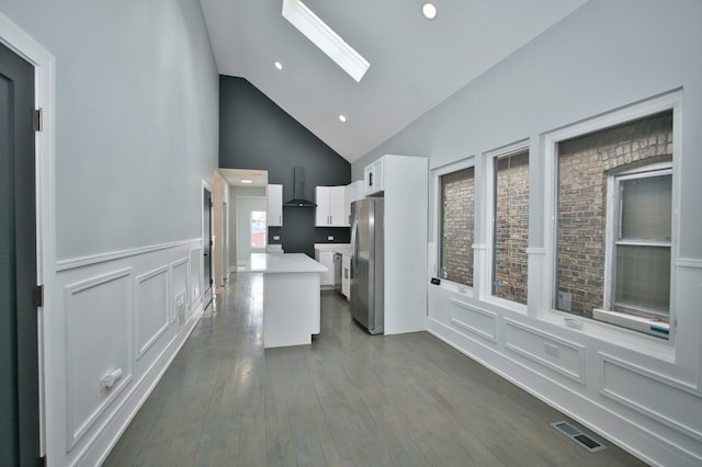 kitchen featuring wall chimney exhaust hood, freestanding refrigerator, visible vents, white cabinetry, and light countertops