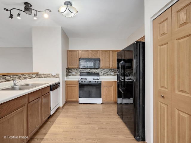 kitchen with tasteful backsplash, light wood-style flooring, a sink, light countertops, and black appliances