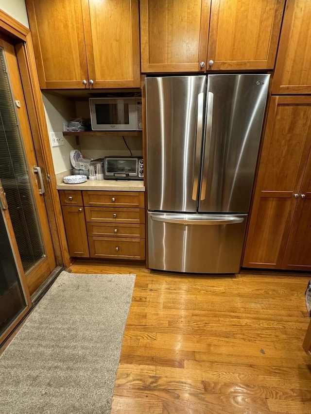 kitchen with brown cabinets, a toaster, stainless steel appliances, light countertops, and light wood-type flooring