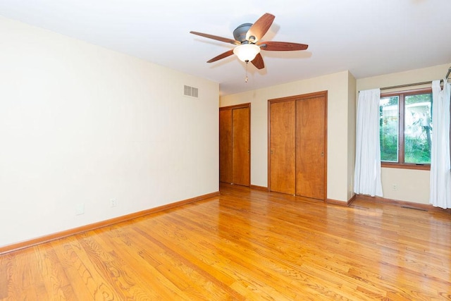unfurnished bedroom with baseboards, visible vents, light wood-style floors, two closets, and ceiling fan
