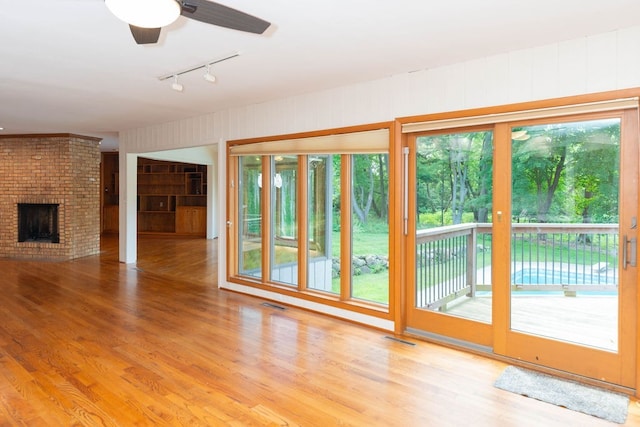 unfurnished living room featuring a ceiling fan, wood finished floors, track lighting, a fireplace, and visible vents