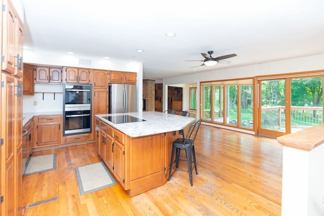 kitchen featuring a center island, light wood-style flooring, a kitchen breakfast bar, ceiling fan, and appliances with stainless steel finishes