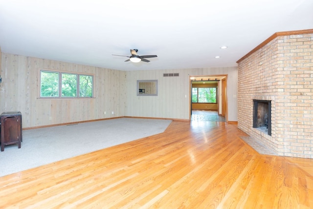unfurnished living room with a ceiling fan, wood finished floors, a fireplace, baseboards, and visible vents